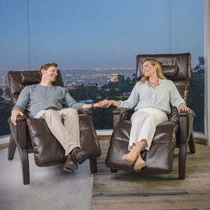 A couple relax in Svago Newton Zero Gravity Recliners, holding hands with a city view behind them.